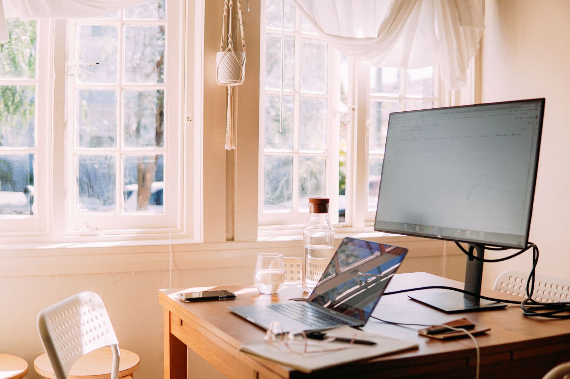 Werkplek met laptop aan een houten tafel, daglicht door een groot raam.